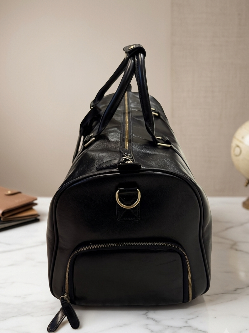 Black leather duffel bag on a marble surface with a beige wall and globe in the background.